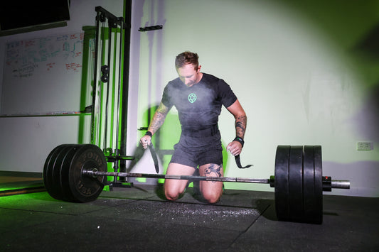 Male athlete behind barbell after clapping hands with chalk, wearing Turtle Strength Weight Lifting Belt, Lifting Straps and Tshirt in Garage Gym Setting with Green light