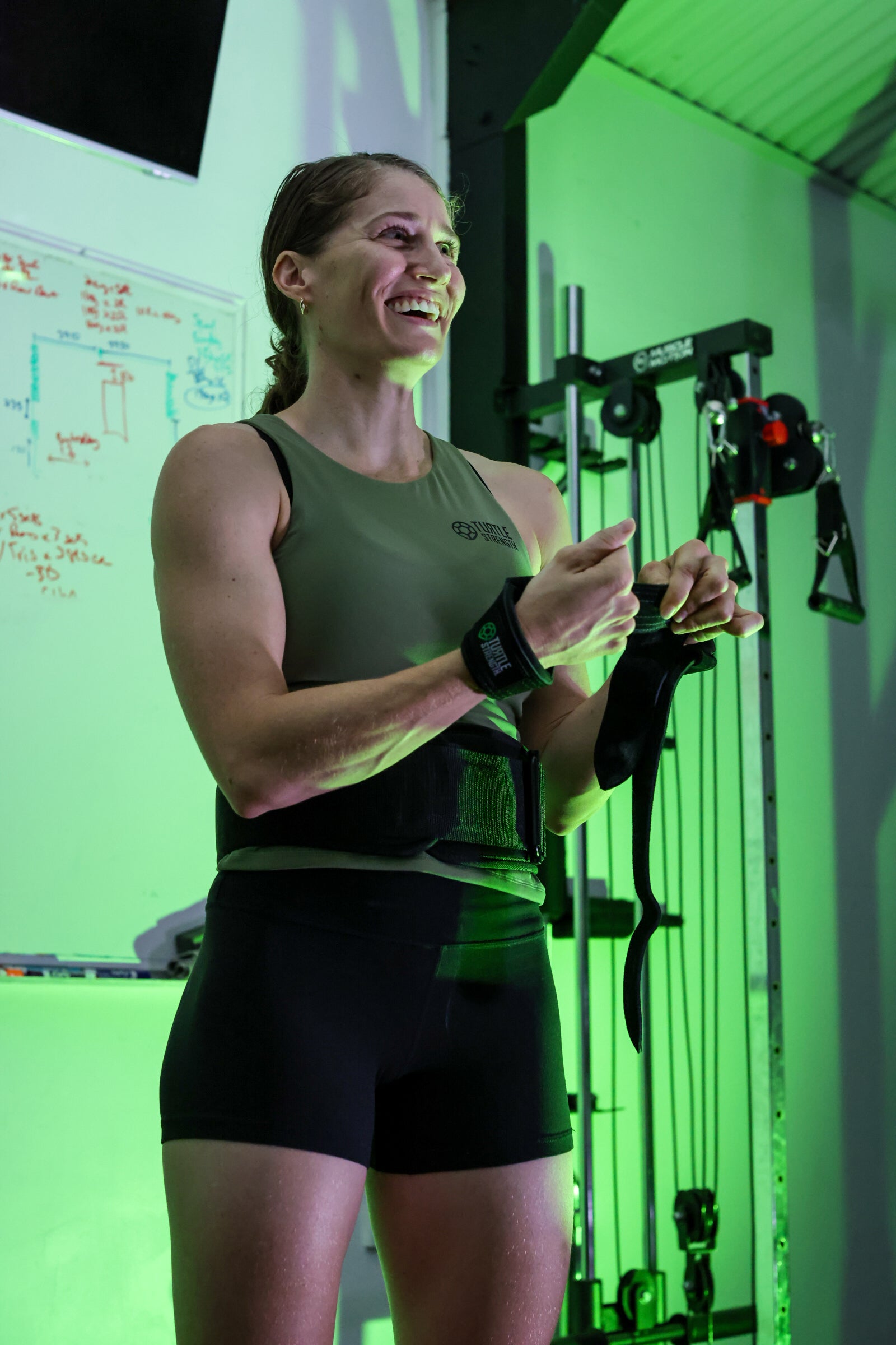 Lady wearing Turtle Strength lifting belt, lifting straps smiling and getting ready to lift weights